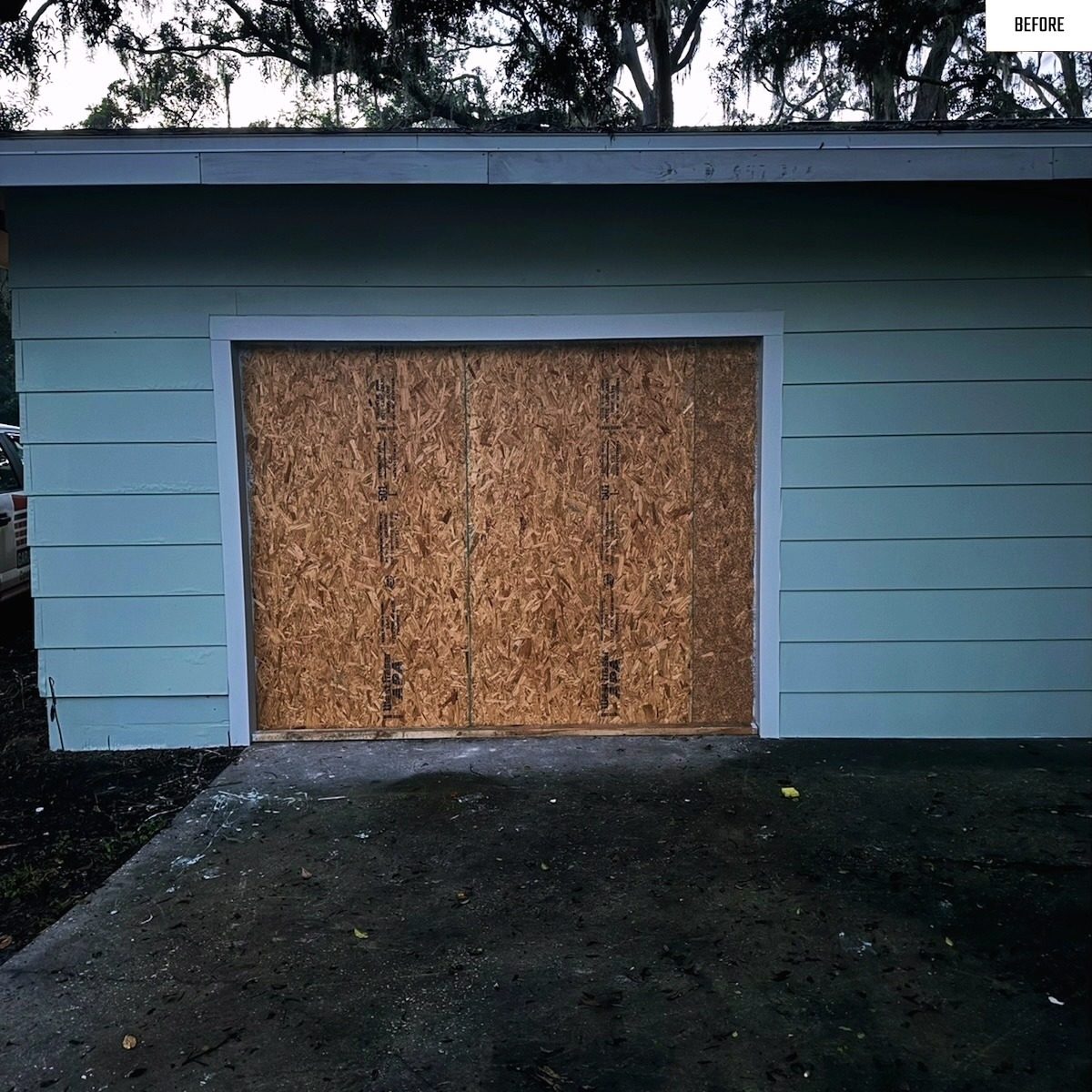 Before: a boarded up garage opening finished with a new white door